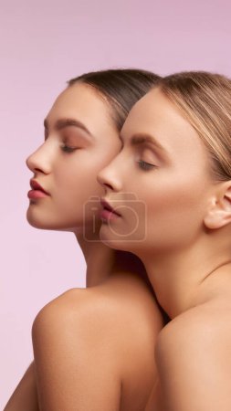 Foto de Blonde and brunette. Portrait of two young, beautiful girls with well-kept skin isolated over pink studio background. Concept of skincare, cosmetology, natural beauty, youth, spa, cosmetics. Ad - Imagen libre de derechos