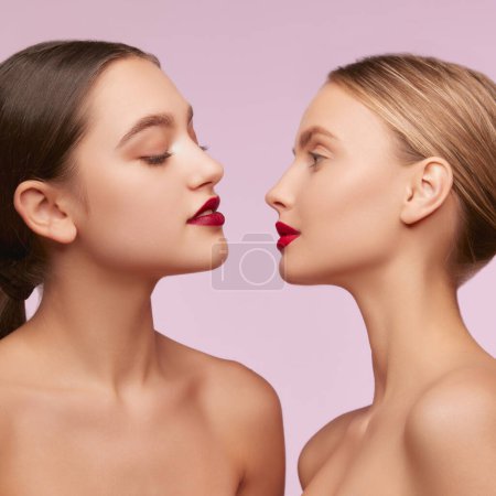 Photo for Red lips. Portrait of two young, beautiful girls with well-kept skin isolated over pink studio background. Concept of skincare, cosmetology, natural beauty, youth, spa, cosmetics. Ad - Royalty Free Image
