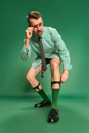 Photo for Portrait of handsome, brutal man, businessman in shirt without pants posing over green studio background. Getting ready for work. Concept of emotions, business, occupation, facial expression, fashion - Royalty Free Image