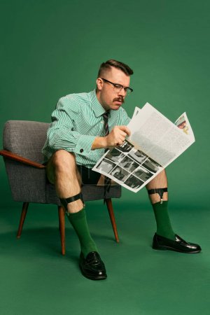 Foto de Morning news briefing. Portrait of handsome businessman in shirt without pants sitting on chair and reading over green studio background. Concept of emotions, business, occupation, facial expression - Imagen libre de derechos