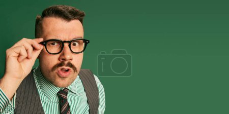 Photo for Questioning look. Portrait of handsome man, businessman in classical suit and lasses posing over green studio background. Concept of emotions, business, occupation, facial expression, fashion - Royalty Free Image
