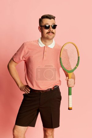 Foto de Joyful. Portraits of handsome charismatic man in stylish clothes posing with tennis racket over pink studio background. Concept of sport, emotions, retro style, lifestyle, fashion. Ad - Imagen libre de derechos