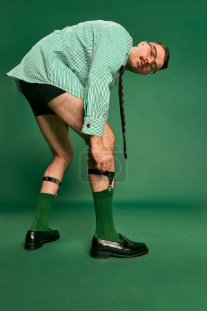 Photo for Portrait of handsome man, businessman in shirt without pants, putting socks on, posing over green studio background. Concept of emotions, business, occupation, facial expression, fashion - Royalty Free Image