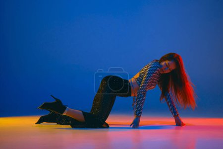 Téléchargez les photos : Self-expression. Young girl dancing high heel dance in stylish clothes over blue background in neon light. Concept of dance lifestyle, modern style, contemporary dance, youth culture, self-expression - en image libre de droit