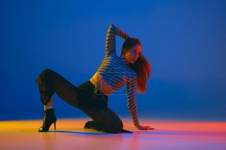 Téléchargez les photos : Passion. Portrait of young girl dancing high heel dance in stylish clothes over blue background in neon light. Concept of dance lifestyle, modern style, contemporary, youth culture, self-expression - en image libre de droit