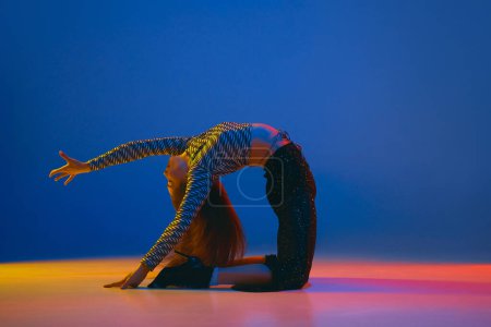 Téléchargez les photos : Portrait of young flexible girl dancing high heel dance in stylish clothes over blue background in neon light. Concept of dance lifestyle, modern style, contemporary, youth culture, self-expression - en image libre de droit