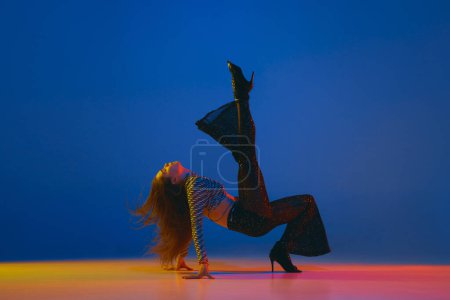 Photo for Portrait of young girl dancing, training heels dance in stylish clothes over blue background in neon light. Concept of dance lifestyle, modern style, contemporary, youth culture, self-expression - Royalty Free Image