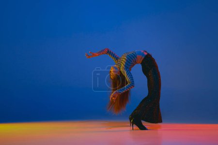 Foto de Flexibility. Young girl dancing heels dance in stylish clothes over blue background in neon light. Concept of dance lifestyle, modern style, contemporary, youth culture, self-expression - Imagen libre de derechos