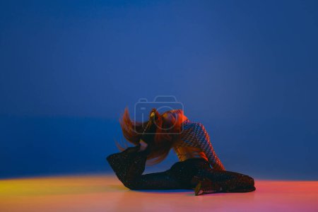 Téléchargez les photos : Flexible passion. Portrait of young girl dancing heels dance in stylish clothes on blue background in neon light. Concept of dance lifestyle, modern style, contemporary, youth culture, self-expression - en image libre de droit