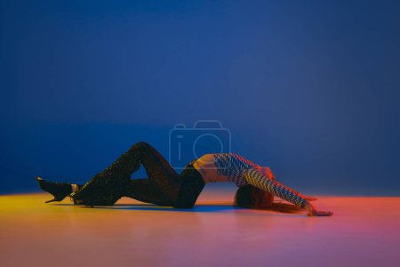 Foto de Hobby. Portrait of young flexible girl dancing heels dance in stylish clothes over blue background in neon light. Concept of dance lifestyle, modern style, contemporary, youth culture, self-expression - Imagen libre de derechos