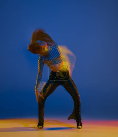 Téléchargez les photos : Dynamics. Portrait of young girl dancing heels dance over blue background in neon light with mixed lights. Concept of dance lifestyle, modern style, contemporary dance, youth culture, self-expression - en image libre de droit
