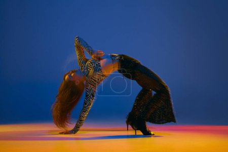 Téléchargez les photos : Flexible move. Young girl dancing heels dance in stylish clothes over blue background in neon with mixed lights. Concept of dance lifestyle, modern style, contemporary, youth culture, self-expression - en image libre de droit