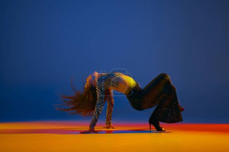 Foto de Flexibility and passion. Young girl dancing heels dance over blue background in neon with mixed lights. Concept of dance lifestyle, modern style, contemporary dance, youth culture, self-expression - Imagen libre de derechos