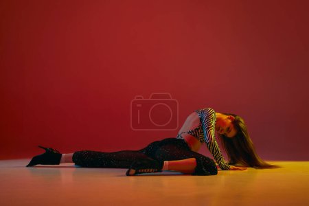 Téléchargez les photos : Warming up movements. Portrait of young girl dancing heels dance over red background in neon light. Concept of dance lifestyle, modern style, contemporary dance, youth culture, self-expression - en image libre de droit