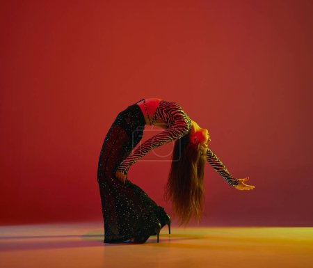 Téléchargez les photos : Flexibility and passion. Portrait of young girl dancing heels dance over red background in neon light. Concept of dance lifestyle, modern style, contemporary dance, youth culture, self-expression - en image libre de droit