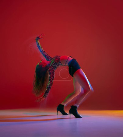 Foto de Flexible impression. Portrait of young girl dancing heels dance over red background in neon light. Concept of dance lifestyle, modern style, contemporary dance, youth culture, self-expression - Imagen libre de derechos