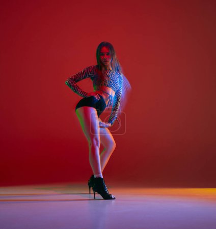 Foto de Portrait of young girl dancing heels dance over red background in neon with mixed light. Concept of dance lifestyle, modern style, contemporary dance, youth culture, self-expression - Imagen libre de derechos
