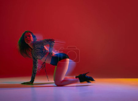 Téléchargez les photos : Passion, femininity. Portrait of young girl dancing heels dance on red background in neon with mixed light. Concept of dance lifestyle, modern style, contemporary dance, youth culture, self-expression - en image libre de droit