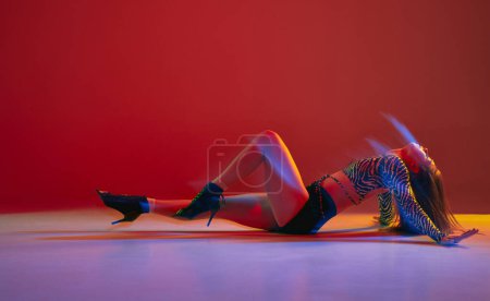 Foto de Passion, femininity. Portrait of young girl dancing heels dance on red background in neon with mixed light. Concept of dance lifestyle, modern style, contemporary dance, youth culture, self-expression - Imagen libre de derechos