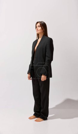 Photo for Portrait of young beautiful girl posing black classic suit over grey studio background. Style. Concept of body and skin care, fitness, natural beauty, health, wellness. - Royalty Free Image
