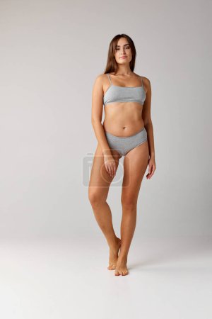 Téléchargez les photos : Self-care. Portrait of young beautiful girl with slim body posing in cotton underwear over grey studio background. Concept of body and skin care, fitness, natural beauty, , wellness. Copy space for ad - en image libre de droit