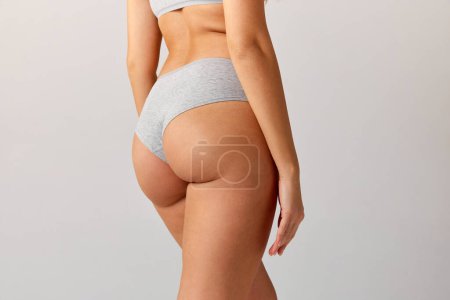 Téléchargez les photos : Cropped image of slim, fit female body, buttocks in cotton underwear over grey studio background. Anti-cellulite care. Concept of body and skin care, fitness, natural beauty, health, wellness. - en image libre de droit