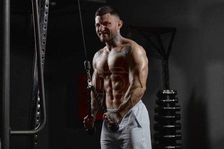 Téléchargez les photos : Portrait of muscular man training shirtless in gym indoors. Doing lat pull down exercises, pulling the rope. Relief, muscular body. Concept of health, sportive lifestyle, fitness, body care, strength - en image libre de droit