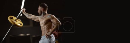 Téléchargez les photos : Portrait of young muscular man training shirtless in gym indoors. Lifting barbell with one hand. Relief body shape. Banner, flyer. Concept of health, sportive lifestyle, fitness, body care, strength - en image libre de droit