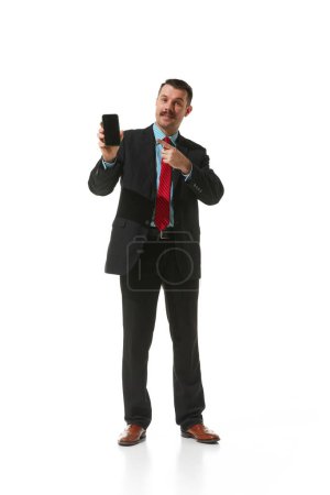 Foto de Businessman in a suit pointing at phone screen over white studio background. Online work, cooperation, assistance. Concept of business, career development, ambitions, innovations. Copy space for ad - Imagen libre de derechos