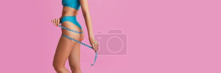 Téléchargez les photos : Cropped image of slim female body over pink background. Model measuring body. Losing weight, diet. Concept of body and skin care, fitness, beauty, health, wellness. Banner, flyer. Copy space for ad - en image libre de droit