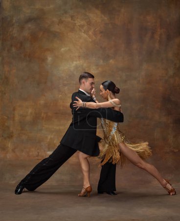 Photo for Attraction, passion, emotions. Man and woman, professional dancers in stylish, beautiful stage costumes performing ballroom dance over dark vintage background. Concept of hobby, lifestyle, action - Royalty Free Image