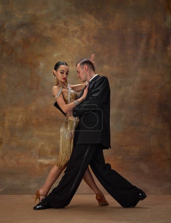 Foto de Man and woman, professional tango dancers in stylish, beautiful stage costumes performing over dark vintage background. Couple dance style. Concept of hobby, lifestyle, action, motion. - Imagen libre de derechos