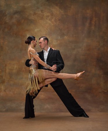 Téléchargez les photos : Sensual pose, attentive look. Man and woman, professional tango dancers in stylish, beautiful stage costumes performing over dark vintage background. Concept of hobby, lifestyle, action, motion. - en image libre de droit