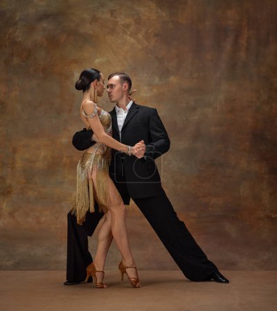 Photo for Deep, impressive look. Man and woman, professional tango dancers in stylish, beautiful stage costumes performing over dark vintage background. Concept of hobby, lifestyle, action, motion. - Royalty Free Image