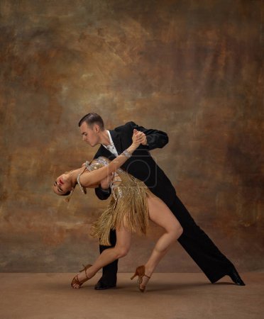 Foto de Man and woman, professional tango dancers in stylish, beautiful stage costumes performing over dark vintage background. Atrraction. Concept of hobby, lifestyle, action, motion, dance aesthetics - Imagen libre de derechos