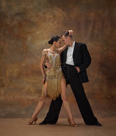 Téléchargez les photos : Man and woman, professional tango dancers in stylish, beautiful stage costumes performing on dark vintage background. Romance and passion. Concept of hobby, lifestyle, action, motion, dance aesthetics - en image libre de droit