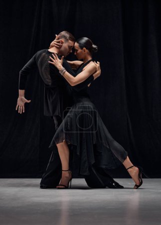 Photo for Passion, romance, emotions. Man and woman, professional tango dancers performing in black stage costumes over black background. Concept of hobby, lifestyle, action, motion, art, dance aesthetics - Royalty Free Image