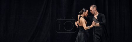 Foto de Man and woman, professional tango dancers performing in black stage costumes over black background. Banner, flyer. Concept of hobby, lifestyle, action, motion, art, dance aesthetics - Imagen libre de derechos