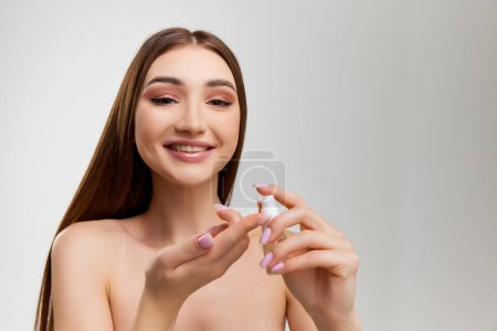 Foto de Beautiful, tender young girl taking care after healthy skin, applying face moisturizing cream over grey studio background. Concept of natural beauty, skin care, cosmetology, cosmetics, health - Imagen libre de derechos