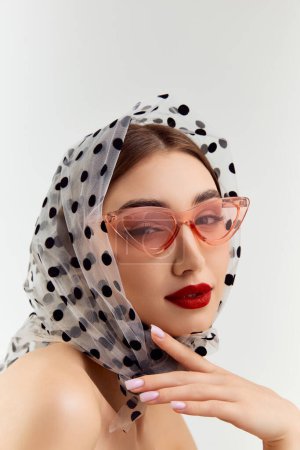 Foto de Sensuality. Beautiful young girl wearing trendy sunglasses and scarf on head, posing over grey studio background. Concept of natural beauty, youth, fashion, cosmetology, wellness, makeup. - Imagen libre de derechos