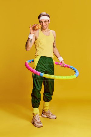 Téléchargez les photos : Choice. Portrait of young cheerful man in sports uniform with croissant and hoop over bright yellow studio background. Concept of emotions, facial expression, sportive lifestyle, retro fashion. Ad - en image libre de droit