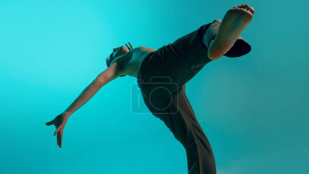 Photo for Bottom view. Contemporary dance style. Young flexible man dancing over blue, cyan studio background. Freedom of movements. Concept of art, body aesthetics, motion, action, inspiration. - Royalty Free Image