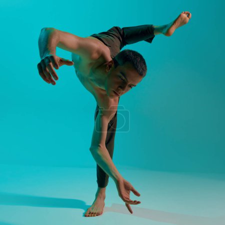 Photo for Bottom view. Contemporary dance style. Young flexible, shirtless man dancing over blue, cyan studio background. Experimental dance. Concept of art, body aesthetics, motion, action, inspiration. - Royalty Free Image