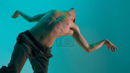 Photo for Bottom view. Contemporary dance style. Young flexible man dancing experimental dance over blue, cyan studio background. Feelings. Concept of art, body aesthetics, motion, action, inspiration. - Royalty Free Image