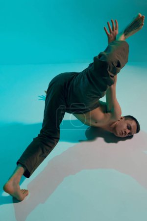 Foto de Contemporary dance style. Young flexible shirtless man dancing experimental dance over blue, cyan studio background. Self-expression. Concept of art, body aesthetics, motion, action, inspiration. - Imagen libre de derechos