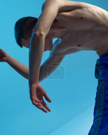 Foto de Contemporary dance style. Young shirtless man dancing contemp, experimental dance over blue studio background. Flexibility. Concept of art, body aesthetics, motion, action, inspiration. - Imagen libre de derechos