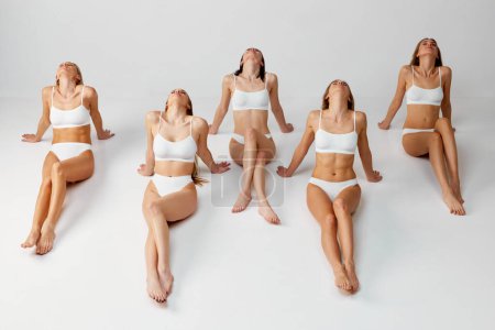 Téléchargez les photos : Pale and tanned body. Group portrait of different beautiful young women posing in white underwear over grey studio background. Natural beauty, body and skin care, diversity, spa, wellness concept. - en image libre de droit
