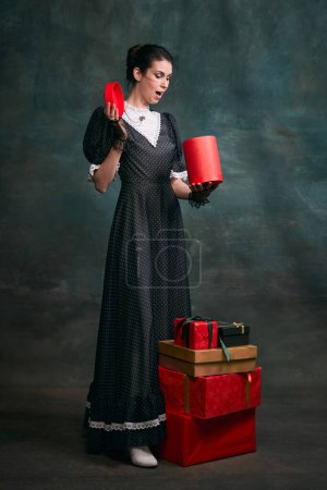 Photo for With present boxes. Young beautiful woman in image of Anna Karenina in retro black dress posing over dark vintage background. Concept of literature character, history, retro style, comparison of eras - Royalty Free Image