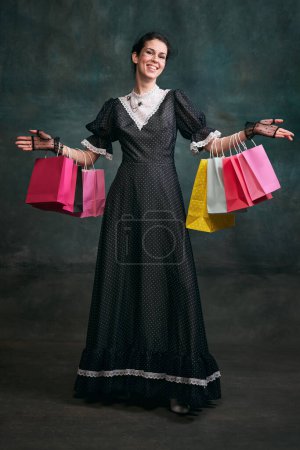 Photo for Shopping. Young beautiful woman in image of Anna Karenina in retro black dress posing over dark vintage background. Sales. Concept of literature character, history, retro style, comparison of eras - Royalty Free Image