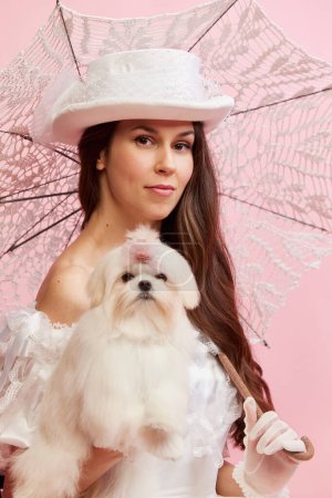Photo for Family look. Portrait of beautiful lady, woman in white vintage dress with umbrella posing with cute dog on pink background. Concept of 19th century, fashion, comparison of eras, history, retro style - Royalty Free Image